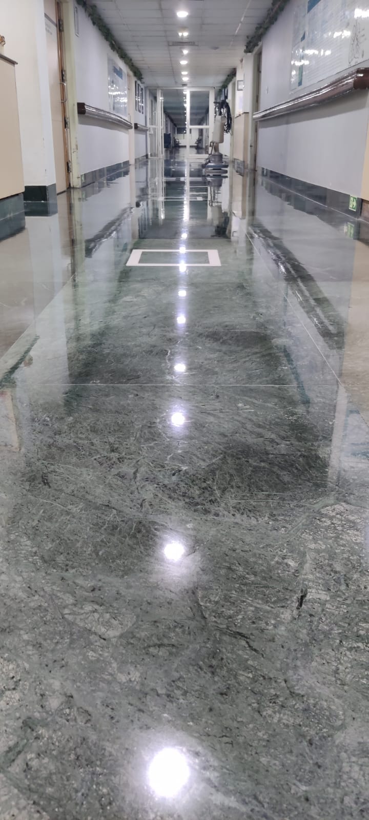 Hospital corridor in green marble reflecting the ceiling lights, floor machine at the far end